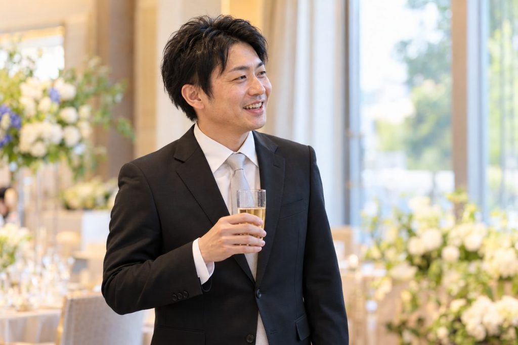 結婚式の会場で黒スーツにシルバーのネクタイを合わせた男性